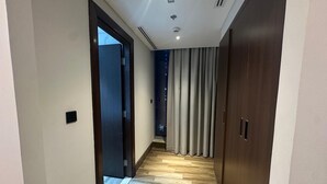 A hallway with wooden flooring, a door on the left, and a window with curtains on the right. - Modern 1BR in J One Pool & Gym (Dubai)