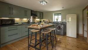 A kitchen with a wooden island, bar stools, a washing machine, and a refrigerator.