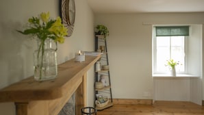 A cozy room with a wooden shelf, a wall clock, a window with a view, and a shelf with decorative items.