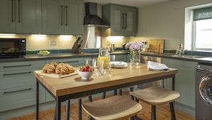 A kitchen with a wooden table, two stools, a microwave, a sink, and a dishwasher.