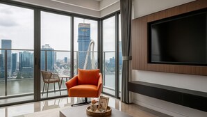 Ein modernes Wohnzimmer mit großem Fernseher, Blick auf die Stadt und einem bequemen orangefarbenen Sessel.
