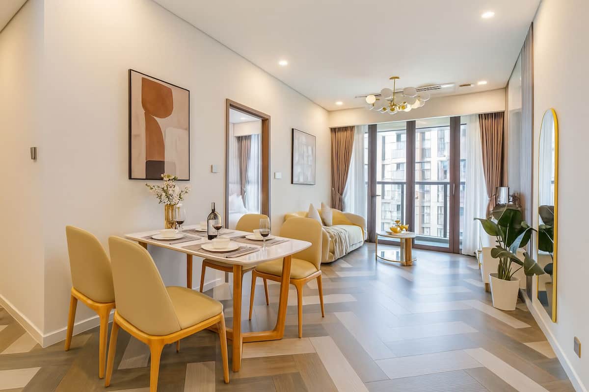 A modern dining area with a long table, yellow chairs, and a chandelier.