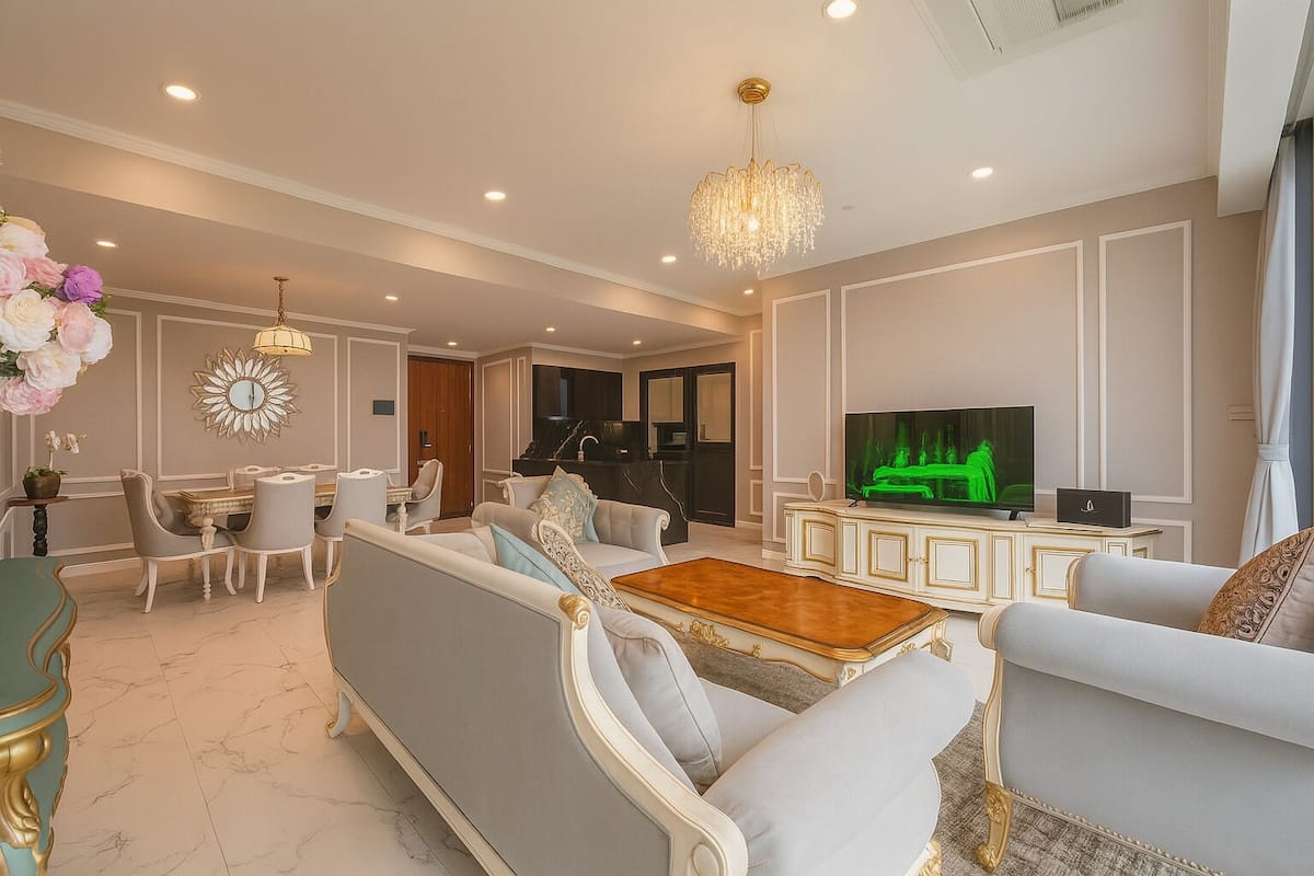 A spacious living room with a large TV, elegant furniture, and a chandelier.
