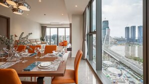 Ein moderner Essbereich mit einem großen Tisch, gedeckt für eine Mahlzeit, mit großen Fenstern, die Blick auf eine Stadtlandschaft und einen Fluss bieten.