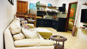 A living room with a sofa, a dining table with chairs, a kitchen area, and a television. - Kazafibi B4 - Steps away from the beach (Flic en Flac)