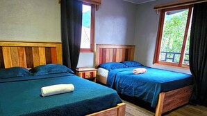 Zwei Holzbetten mit blauer Bettwäsche, ein Holz-Kopfteil, ein Fenster mit Vorhängen und ein Deckenventilator.