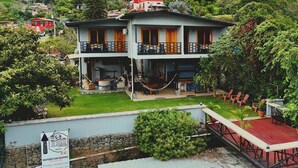 Ein zweistöckiges Gebäude mit Balkon, umgeben von üppiger Vegetation und Hügeln.