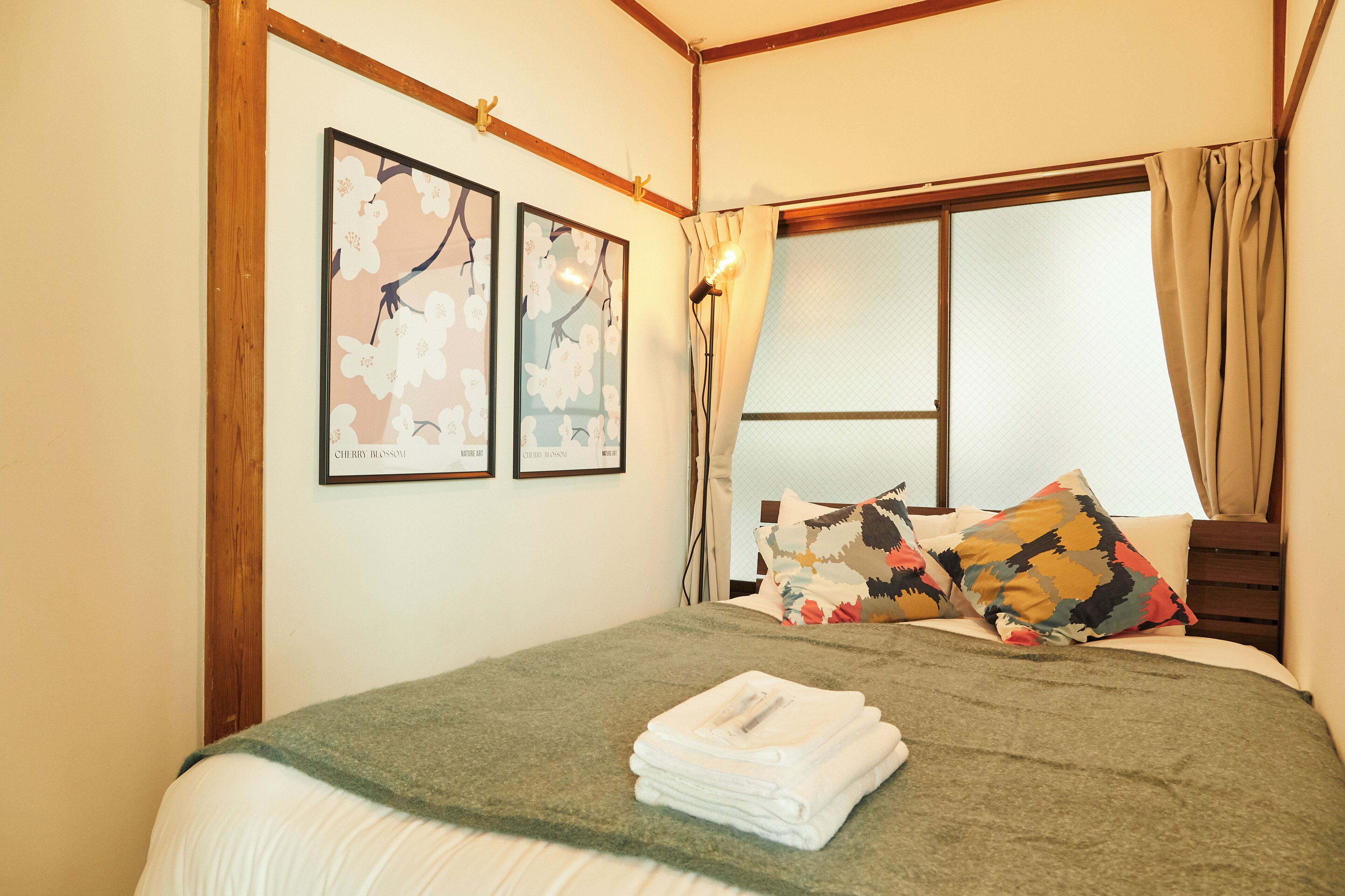 Een slaapkamer met een bed, een raam met gordijnen en twee kunstwerken in een lijst op de muur.