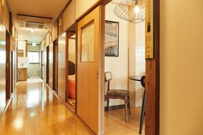 A hallway with wooden flooring, sliding doors, and a chair near a wall-mounted light fixture. - Nisshin Geppo (Kawasaki)