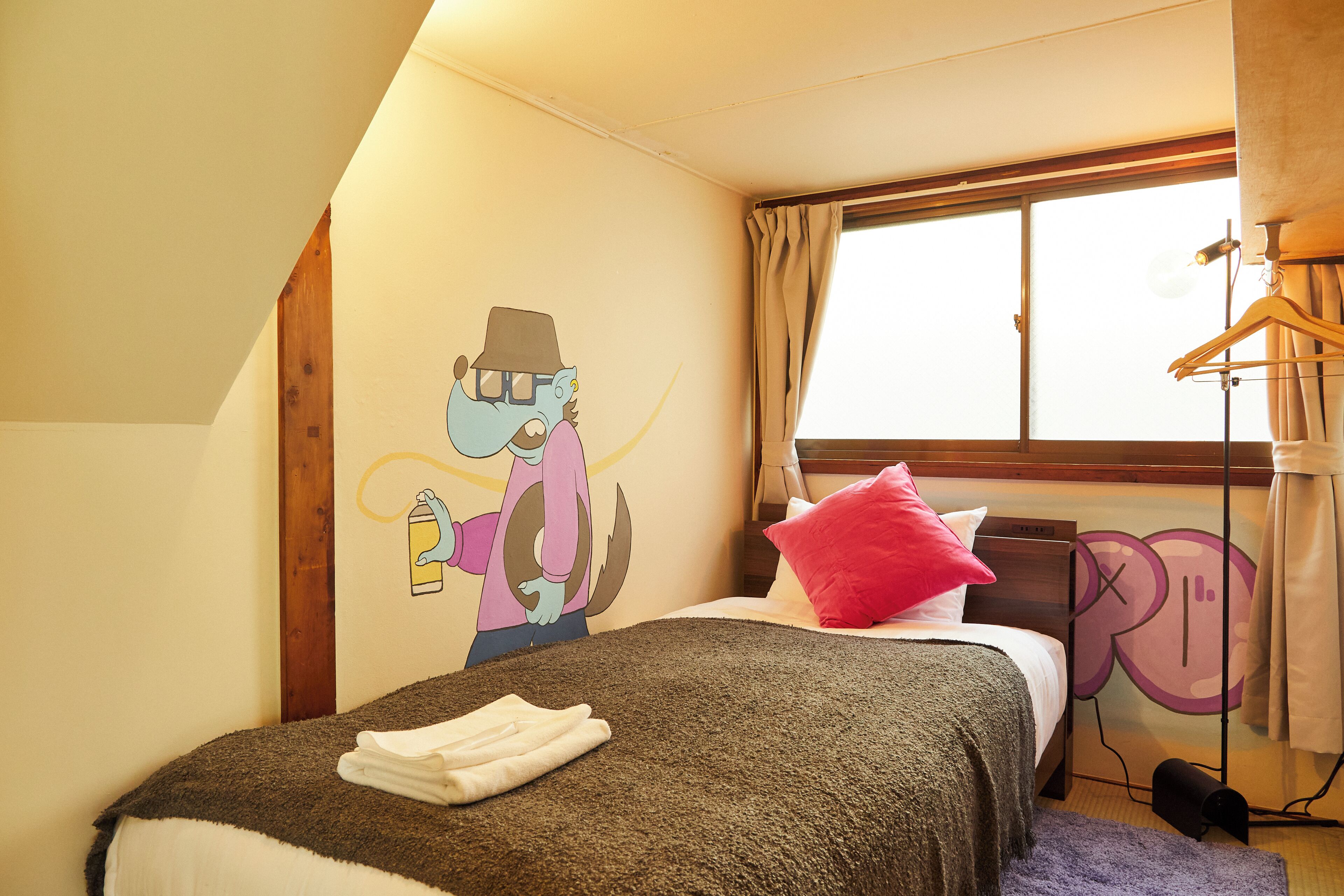 A bedroom with a bed, a wall mural, a window with curtains, and a hanging light fixture.