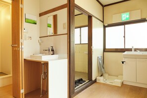 A hotel bathroom with a wooden door, a sink, a mirror, and a shower area. - Nisshin Geppo (Kawasaki)