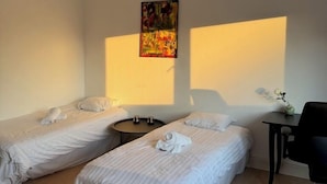A hotel room with two single beds, a small round table, a desk with a chair, and a hanging light fixture.
