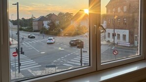 A view from a window overlooking a street at sunset with buildings and cars.