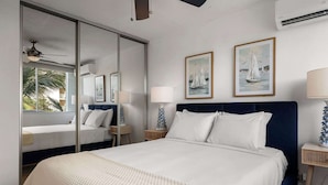 Habitación de hotel con una cama grande, ventilador de techo, ventana con vistas a palmeras y dos cuadros en la pared.