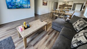 Un salon moderne avec un plancher en bois, un canapé gris, une table basse et un tableau accroché au mur.