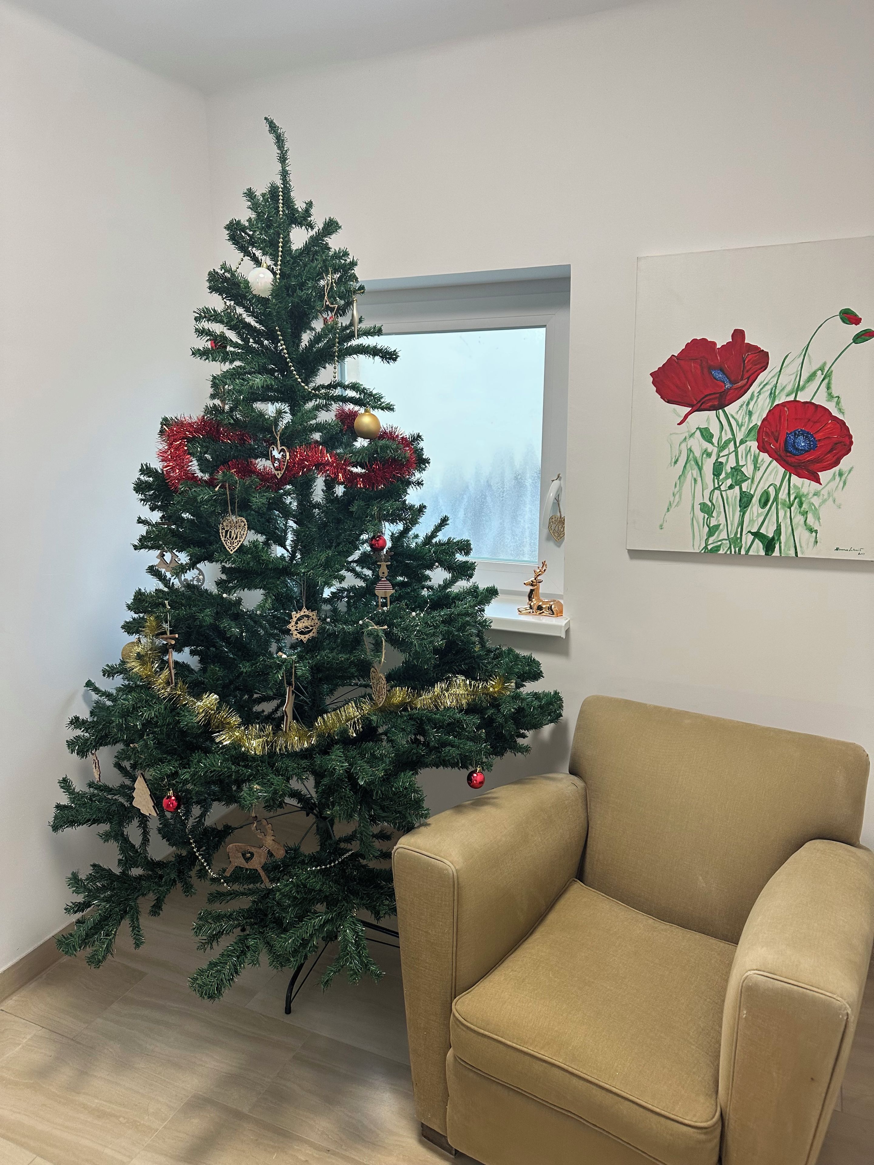 A room with a Christmas tree, a beige armchair, and a painting on the wall.