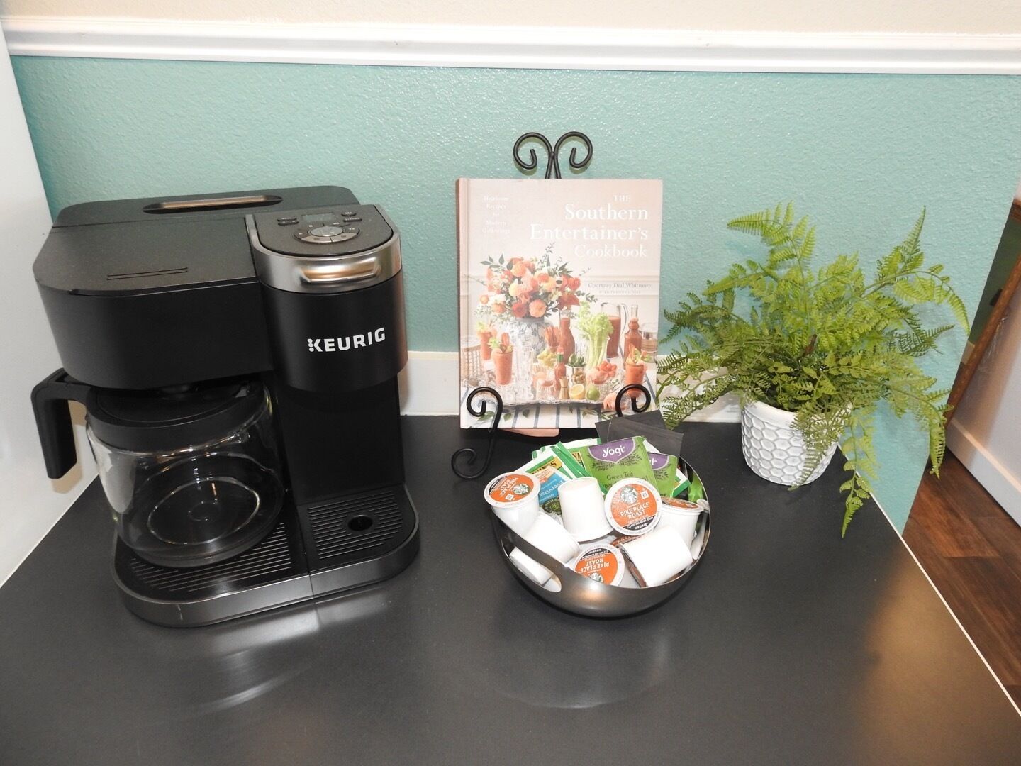 A KEURIG coffee maker, a book titled 'The Southern Entertainer's Cookbook', and a basket of coffee pods on a table.