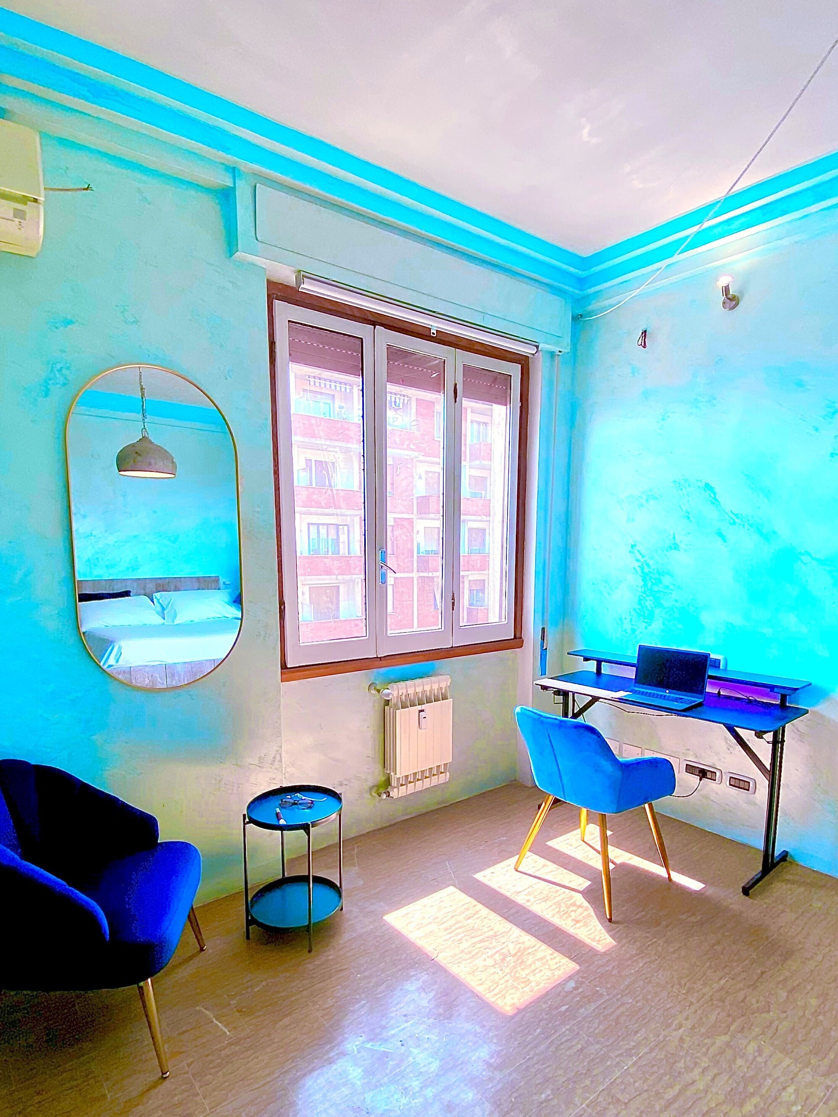 Una habitación con escritorio, dos sillas, radiador, ventana y espejo.