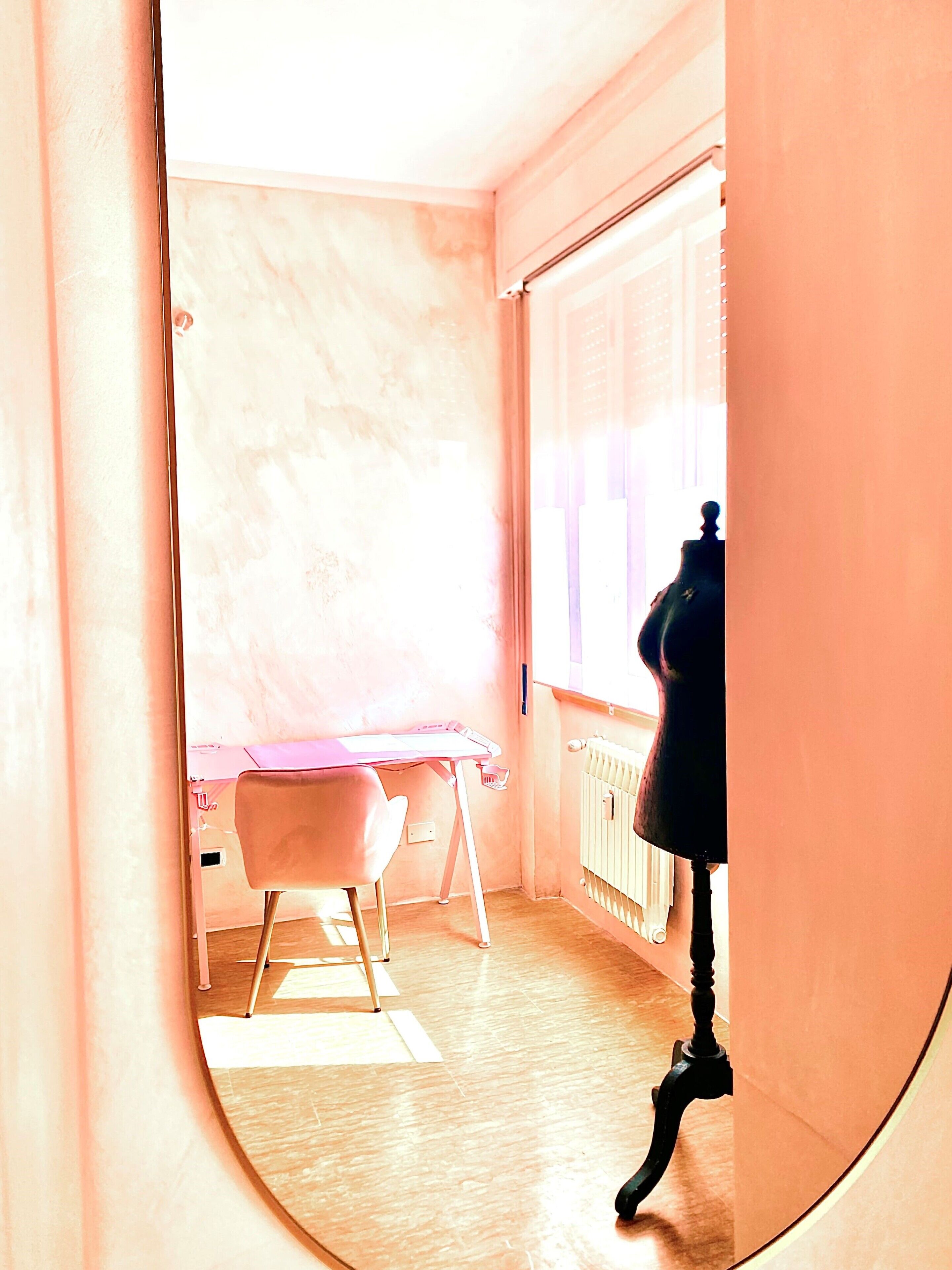 Ein Zimmer mit einem rosa Schreibtisch, einem Sessel und einer Heizung.