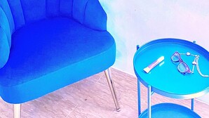 A room with a blue armchair, a small round table with sunglasses and a necklace, and a mirror reflecting a wardrobe and a cabinet. - Bed and Dreams (Florence)