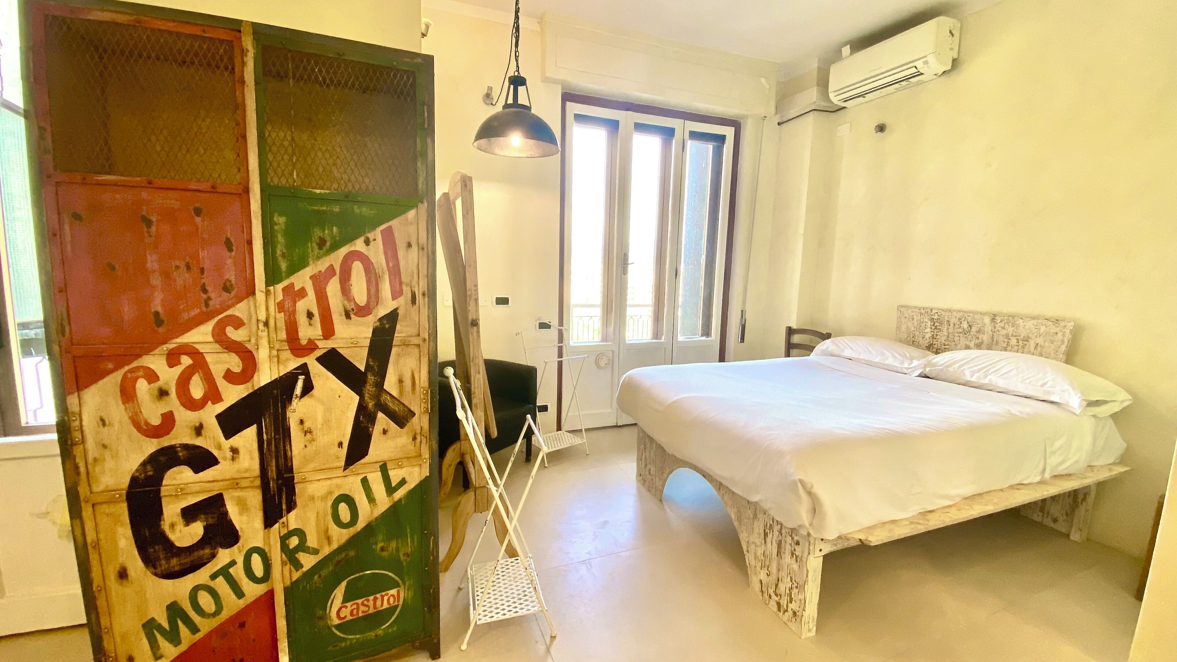 A bedroom with a bed, a hanging light, a door, and an air conditioning unit.