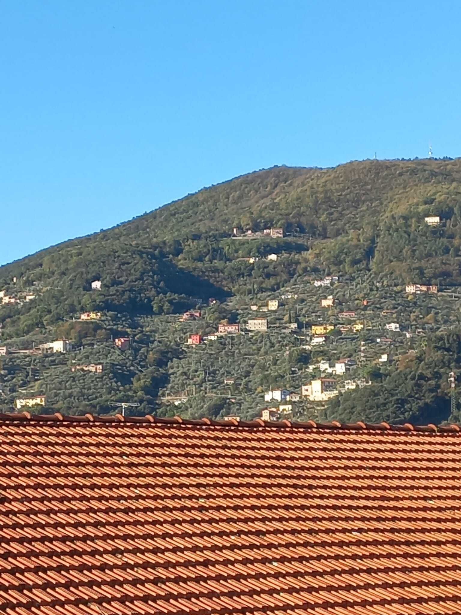 Ein Hügel mit vereinzelten Gebäuden, vermutlich Wohnhäuser, unter blauem Himmel.