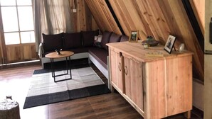 A cozy loft-style room with a sloped ceiling, a sectional sofa, a wooden cabinet, and a small round table. - Amazing 2 bedroom house with WiFi in Gangtok A frame cottage,  peaceful place (Gangtok)