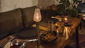 A cozy room with a rustic decor, including a woven wall hanging, various hanging ornaments, and a table set with a candle, plates, and a bowl of snacks. - Amazing 2 bedroom house with WiFi in Gangtok A frame cottage,  peaceful place (Gangtok)