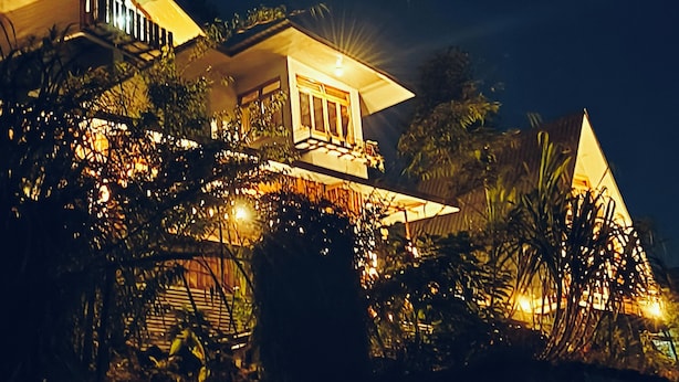 A multi-level house with illuminated balconies and a prominent central window, surrounded by dense foliage. - Amazing 2 bedroom house with WiFi in Gangtok A frame cottage,  peaceful place (Gangtok)
