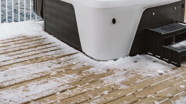 Un jacuzzi en una terraza de madera con vistas a árboles y una masa de agua al fondo.
