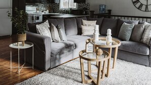 Una sala de estar moderna con un sofá gris, dos mesitas auxiliares y un reloj decorativo en la pared.