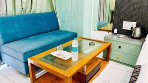 A room with a blue sofa, a glass-top coffee table with a bottle and glasses, a green dresser, and a mirror.