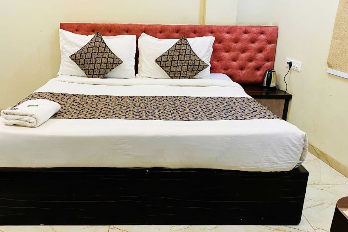 A neatly made bed with a red headboard, white and patterned pillows, and a folded towel on the footboard.