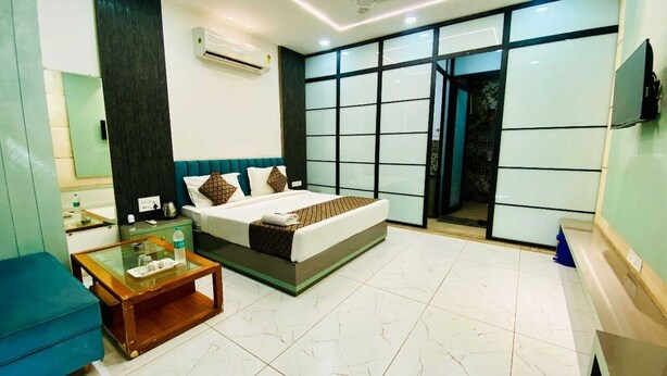 A modern hotel room with a large bed, a glass coffee table, a blue sofa, and a view of the outside through a large window.