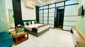 A modern hotel room with a large bed, a glass coffee table, a blue sofa, and a view of the outside through a large window. - Hotel Mura Indore (Indore)