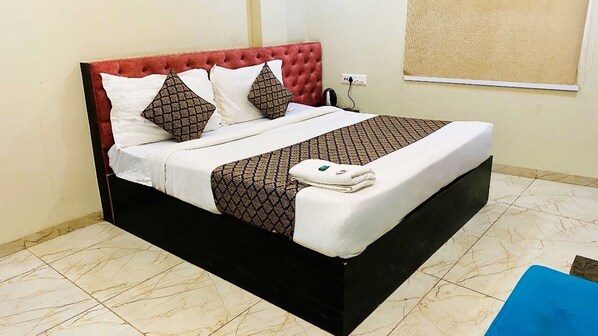 Cama bem arrumada com cabeceira vermelha, roupa de cama branca e cobertores estampados.