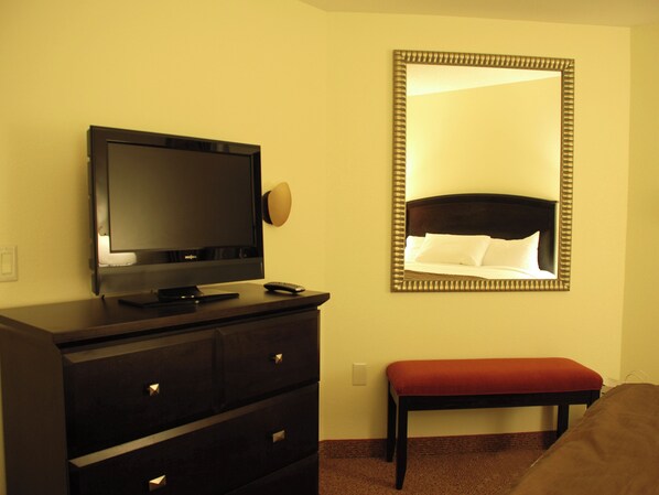 Une chambre d’hôtel avec un téléviseur posé sur une commode, un grand miroir au mur et un banc rouge.