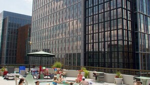 Un edificio moderno con fachada de vidrio y un área de piscina donde personas están relajándose.