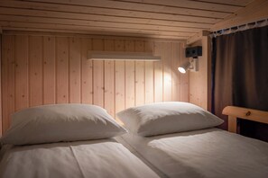 Et værelse med to senge, trævægge, en loftlampe og et vindue med gardiner.