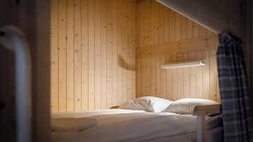 Una cama tipo litera con un panel de madera, un estante pequeño y una cortina escocesa.