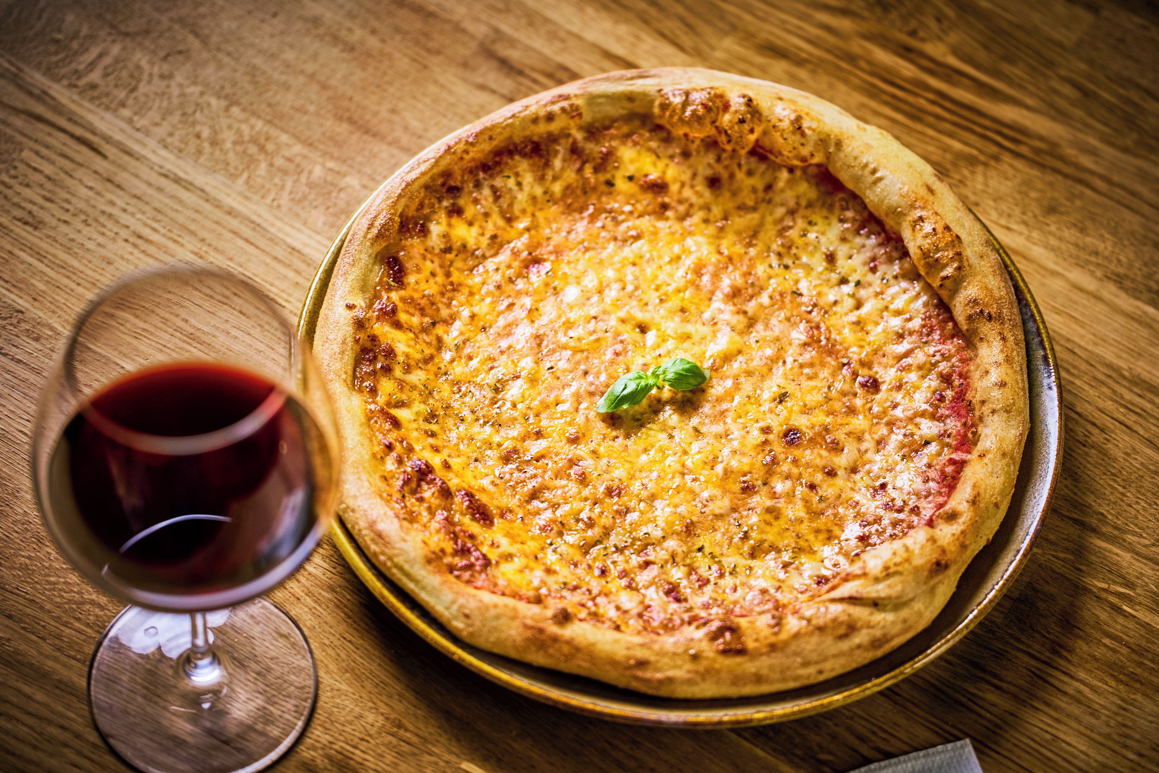 A pizza on a round metal tray on a wooden table.