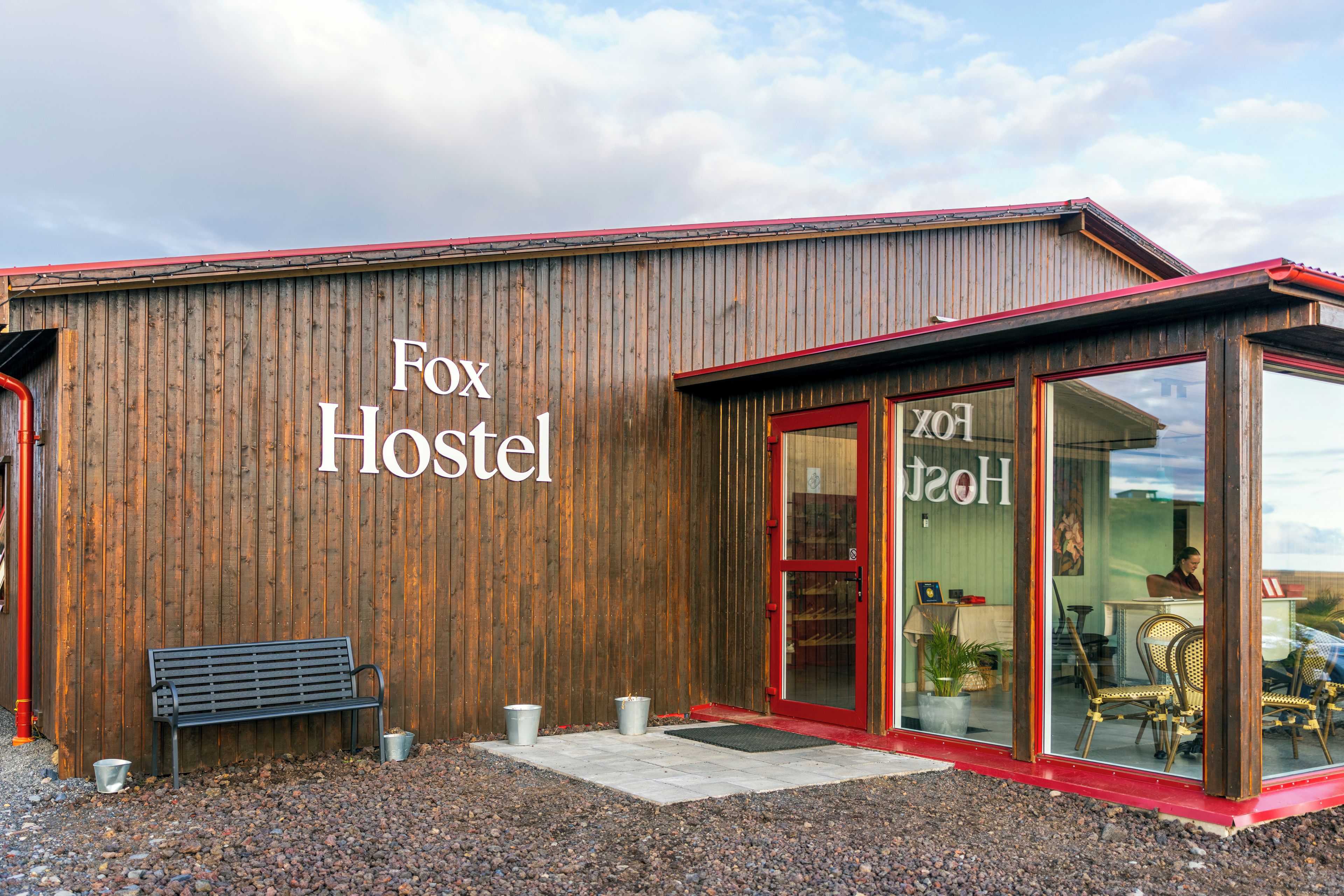 Un edifici de fusta amb un rètol que diu 'Fox Hostel' i una panxa de banc a l'exterior.