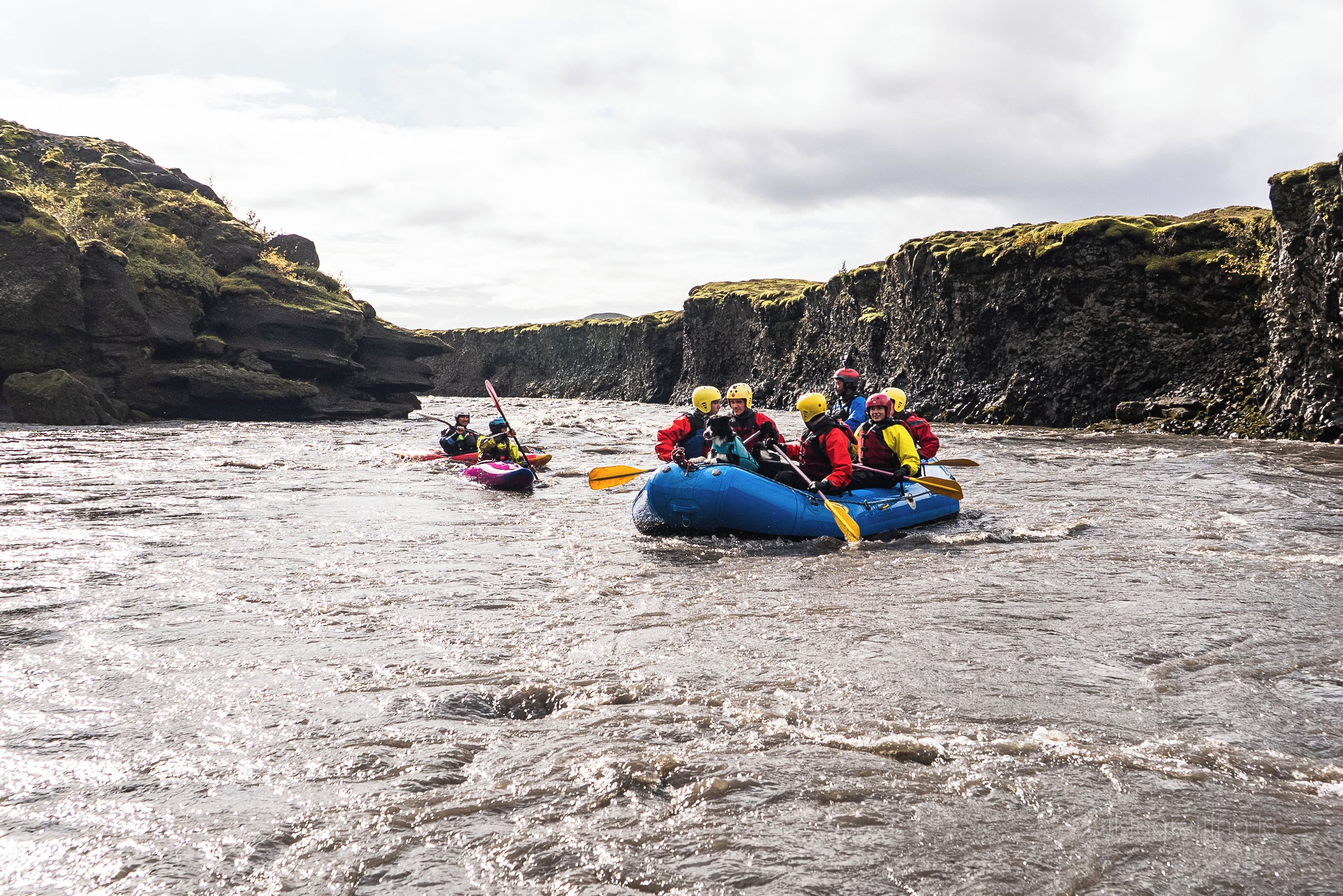 Een groep mensen die op een raft een rivier afdaalt, omringd door rotsachtige kliffen.