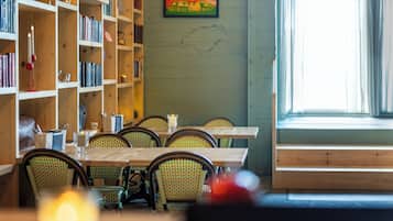 A dining area with wooden tables and chairs, a bookshelf with books, and a painting on the wall.