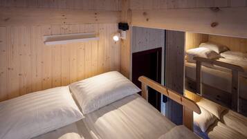 Une chambre avec un lit superposé, des murs en bois et une petite table de chevet.