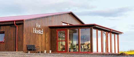 A rustic building with a sign reading 'Fox Hostel' and a large glass door entrance.