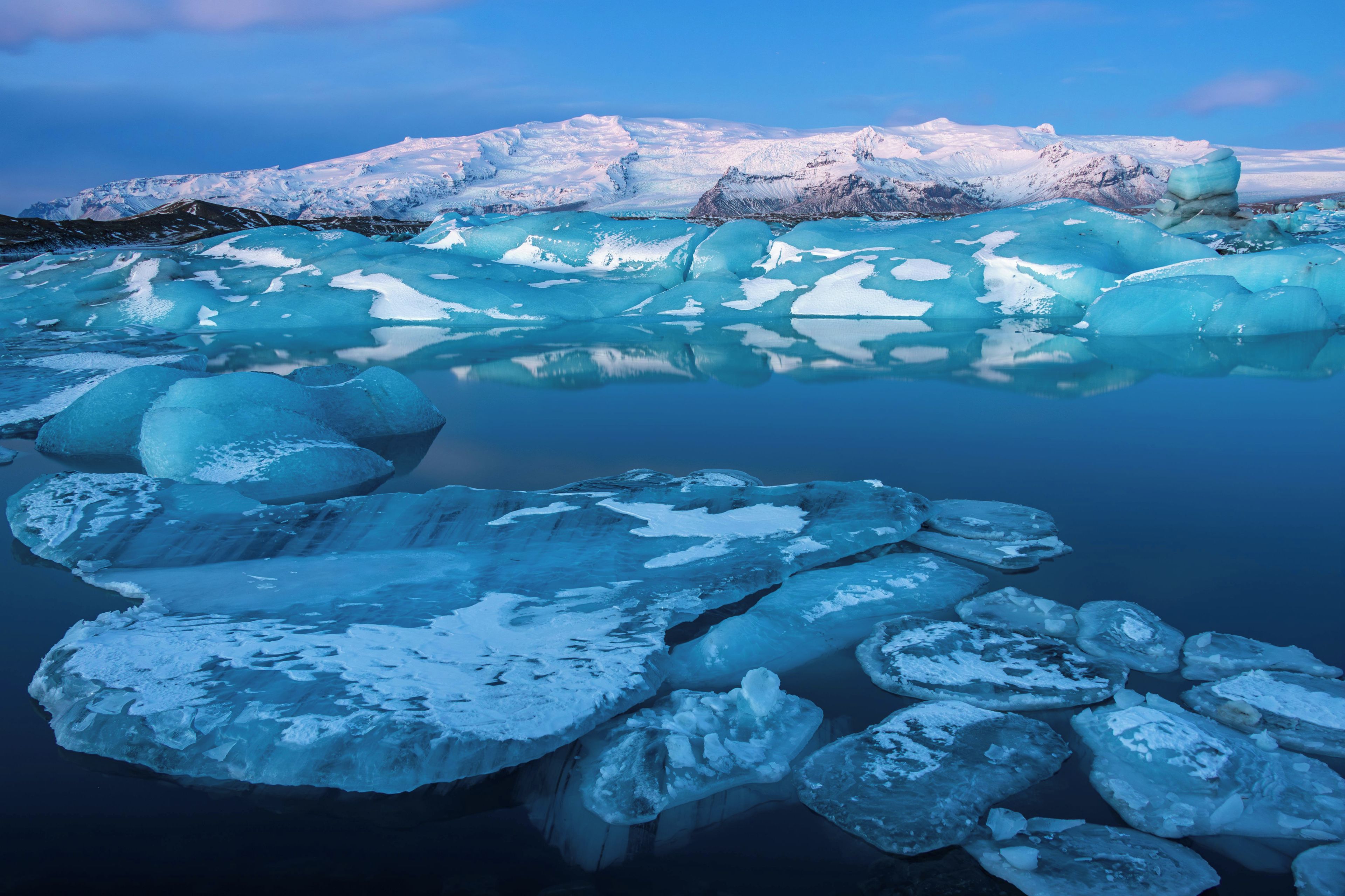 Un glaciar con icebergs flotando en una masa de agua tranquila, reflejando el cielo y el paisaje circundante.