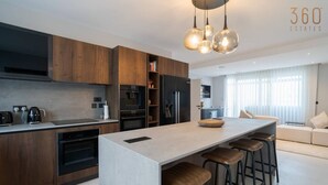 A modern kitchen with wooden cabinets, a central island with stools, and a dining area with a sofa and a table. - 2BR Penthouse Paradise w/ Jacuzzi & BBQ in Sliema (Sliema)