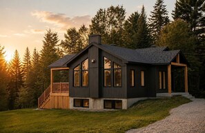Une maison moderne dotée d’une grande terrasse, d’une cheminée et offrant une vue sur la forêt.