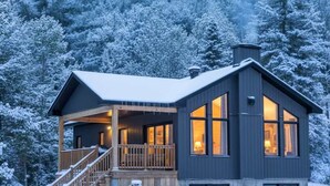 A modern cabin with a wooden deck and large windows, surrounded by snow-covered trees. - Spa, Mountain and River | Le Zenith (Saint-Côme)